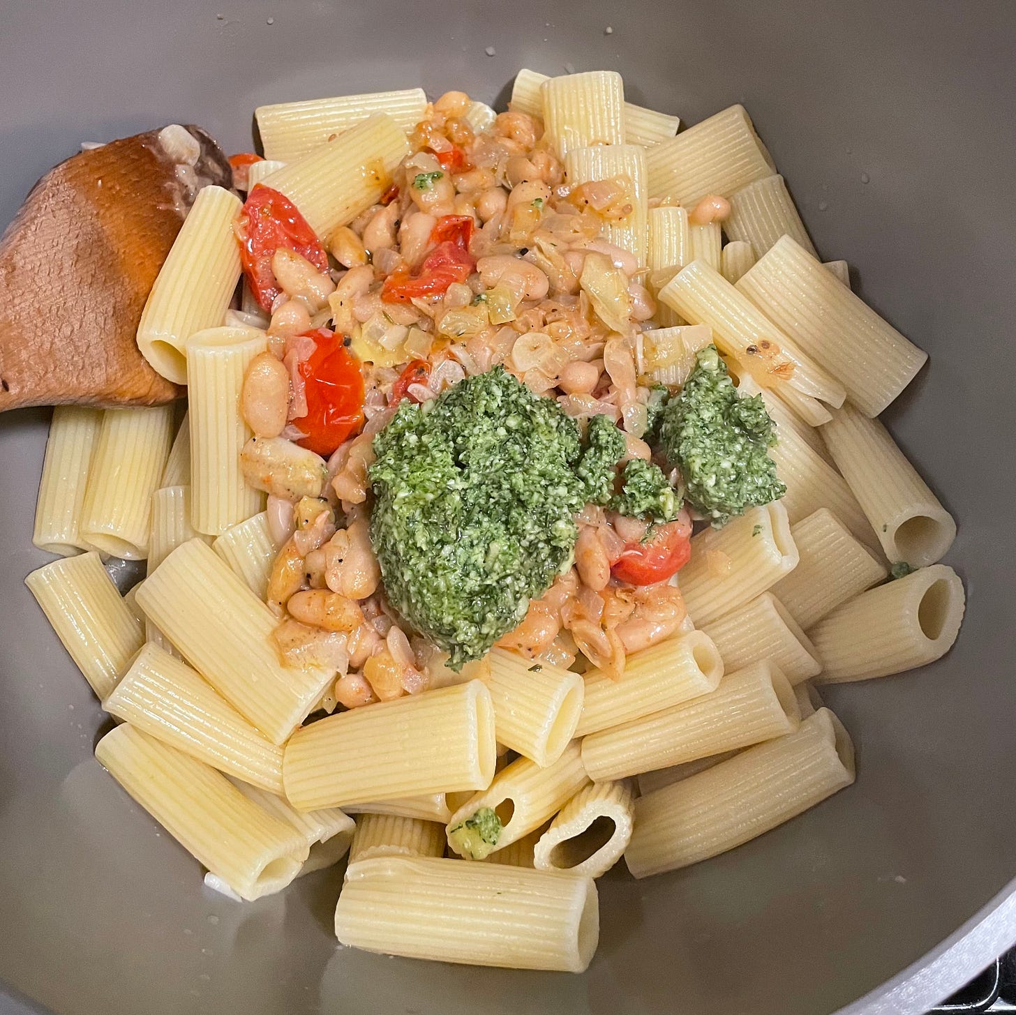 pot of rigatoni with white beans, tomatoes, pesto dolloped in the middle