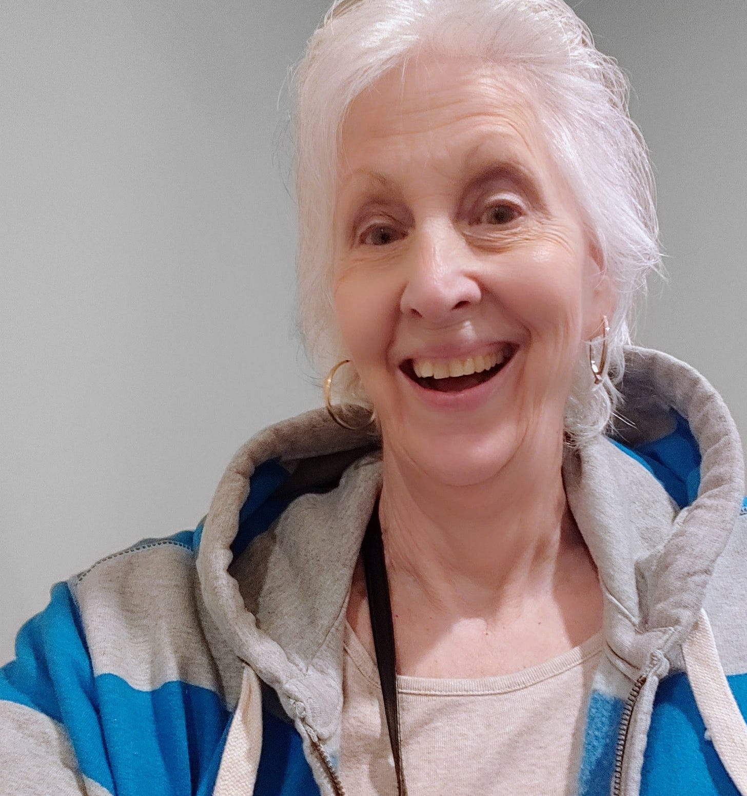 author selfie with blue and grey hoodie, smiling with bright white hair and gold earrings