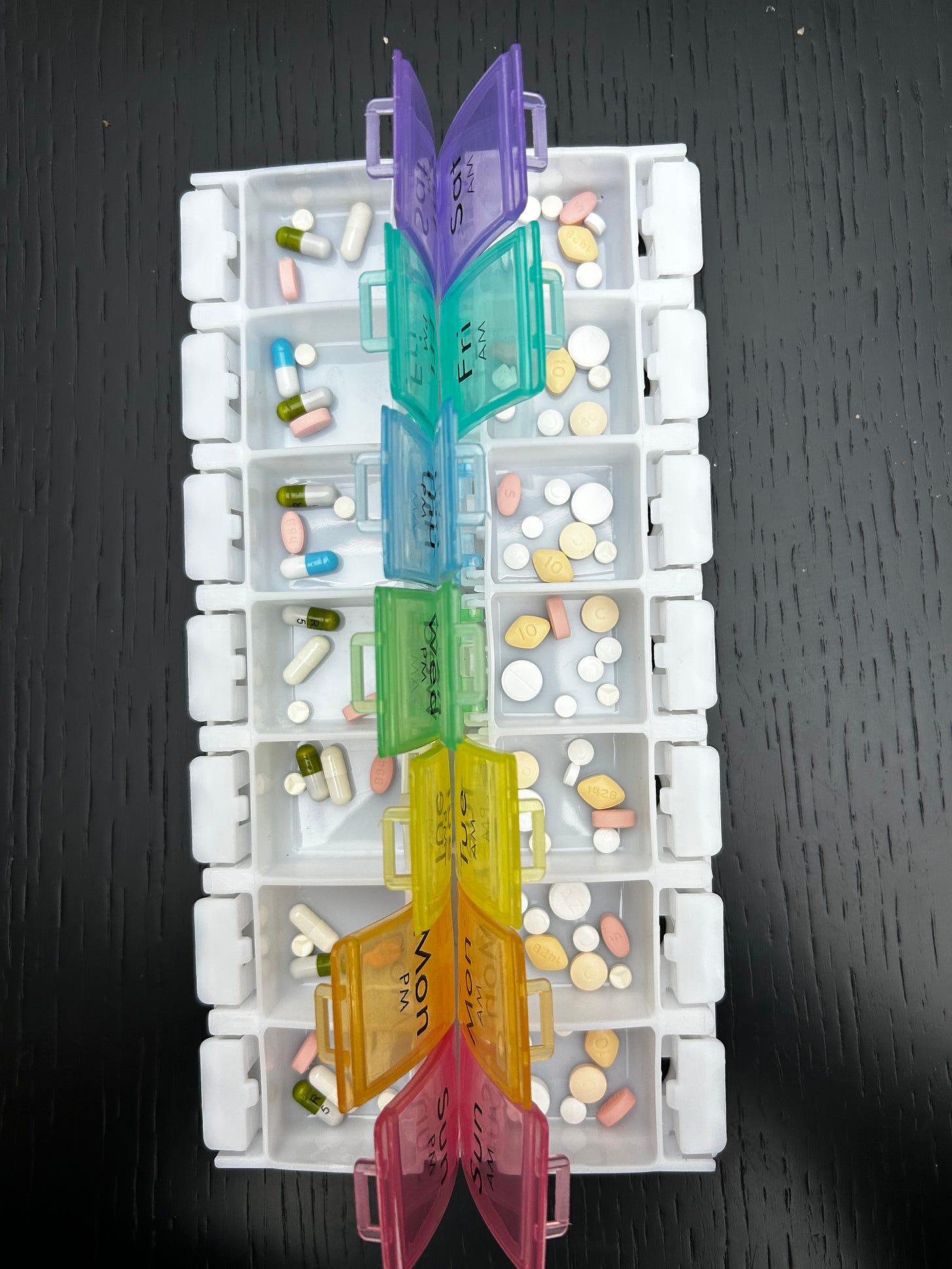 Pill box full of different tablets, with rainbow-colourd lids that are open.