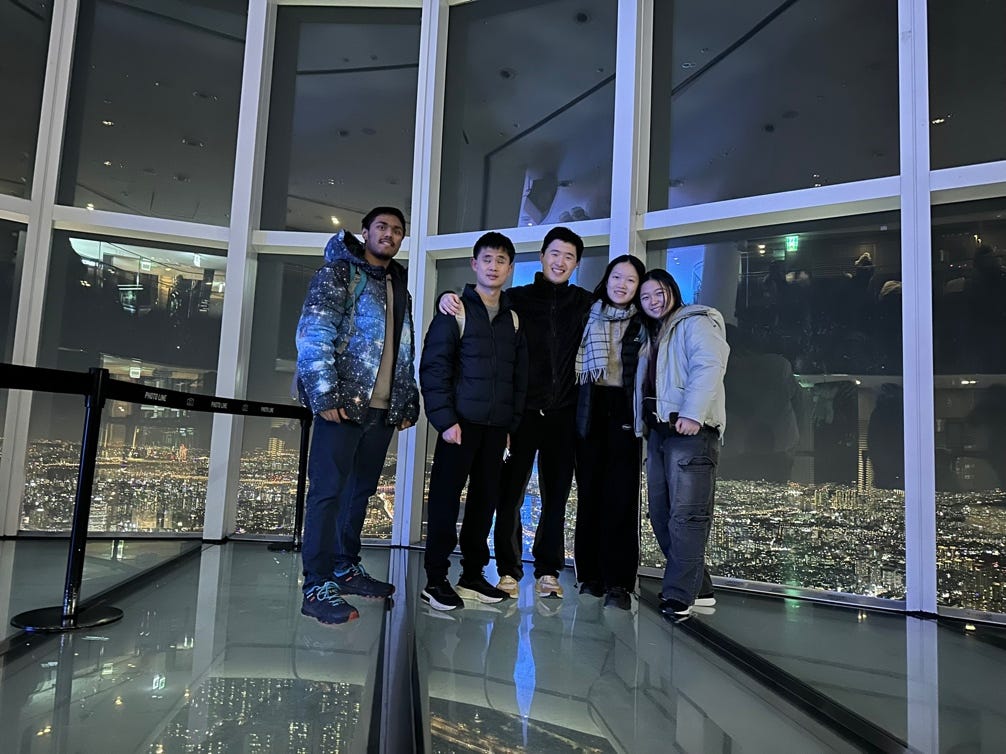 A group of people standing in a room with a view of a city

Description automatically generated