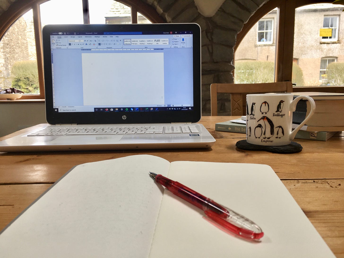 Notebook, pen, laptop and coffee mug on a kitchen table