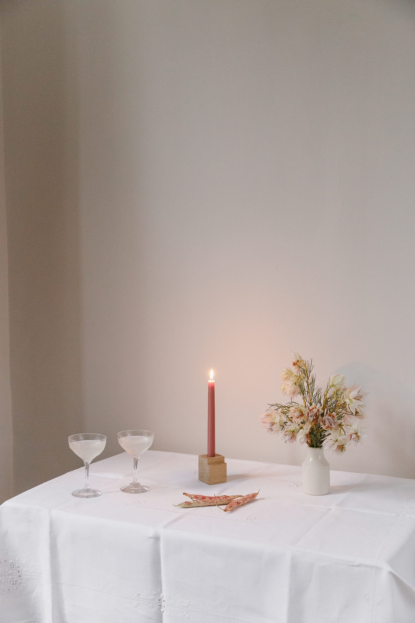 A table set in the corner of a home with two glasses of champagne, a lit candle and a vase of beautiful flowers.