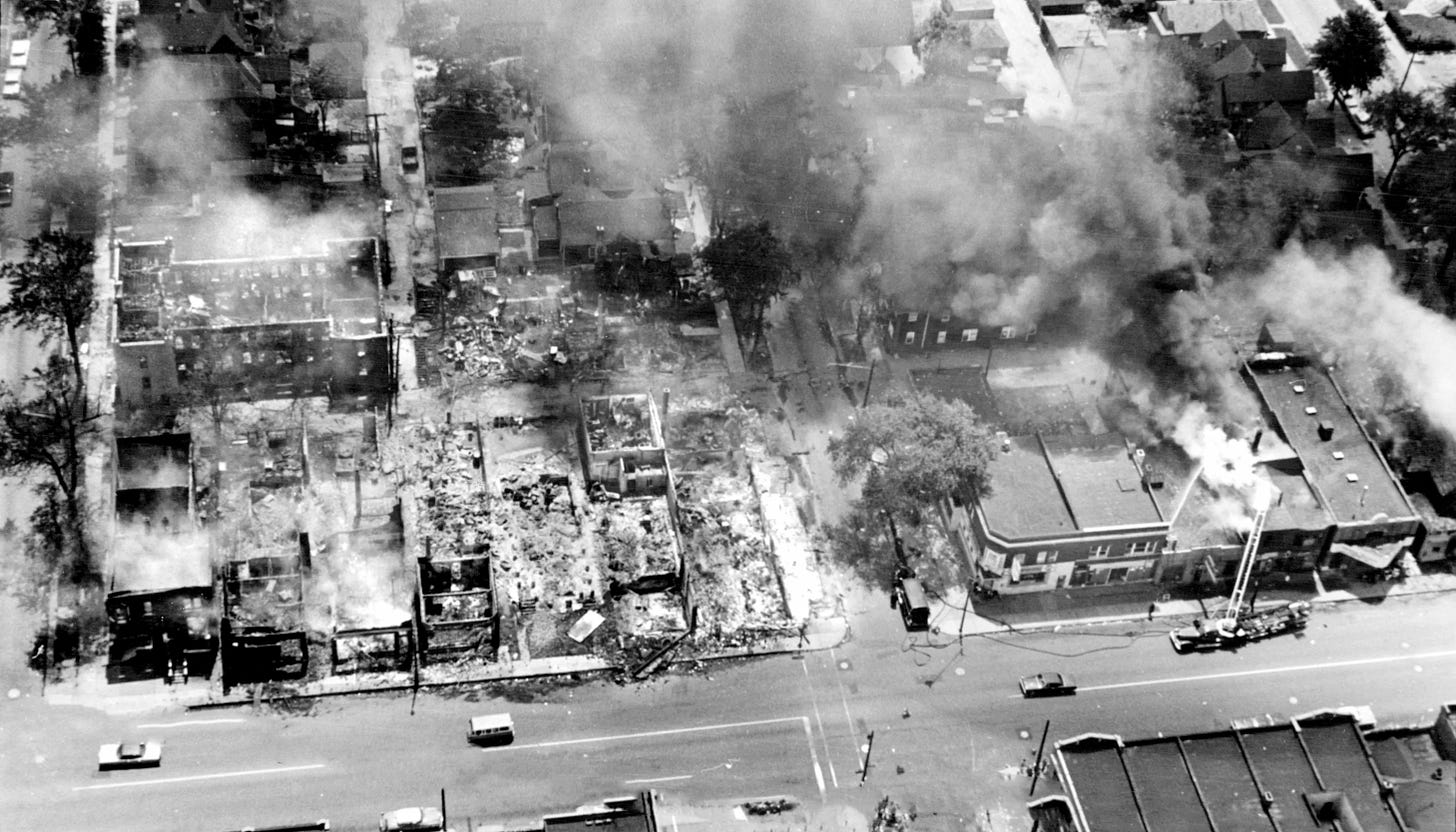 Aerial view of four blocks of destroyed Detroit, one block roofless rubble, the rest smoldering.