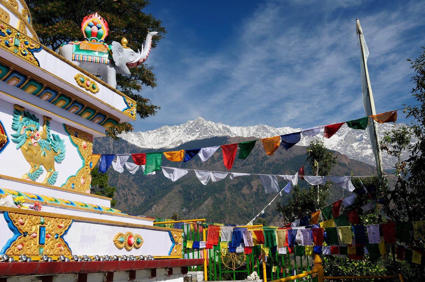 View of temple's corner, colorful elephant statue on roof, prayer flags flying, and mountains in background