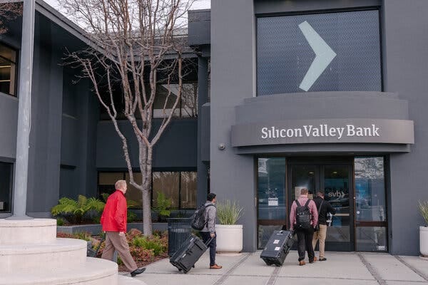 Four men carrying cases and walking into a building with a Silicon Valley Bank sign.