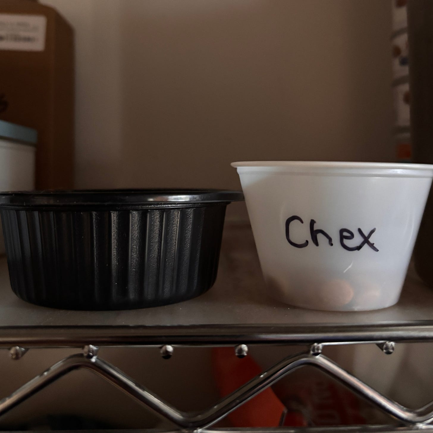 2 small plastic containers sit on a shelf. One says "Chex" The other is black