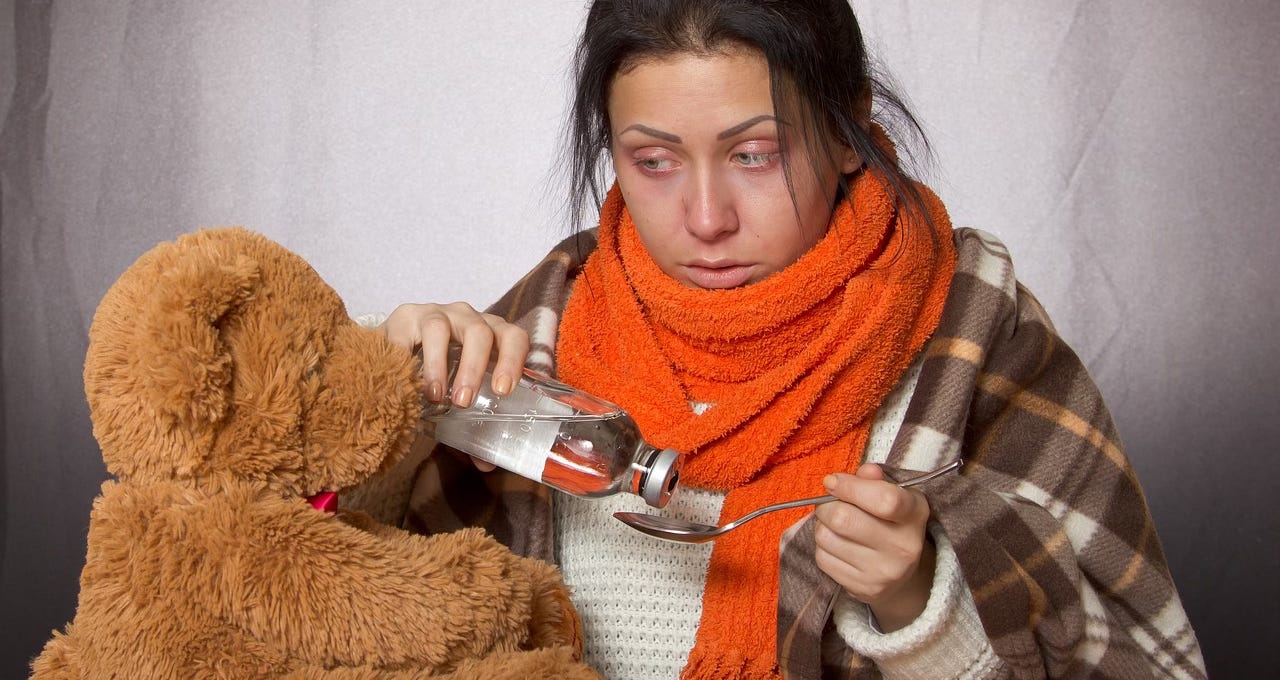 A sick woman pours some medicine onto a spoon for a teddy bear.