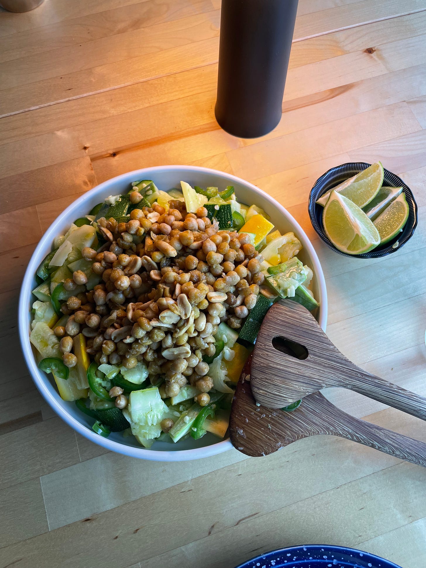 Zucchini salad in a white serving dish topped with fried chickpeas and peanuts, with a side of lime wedges