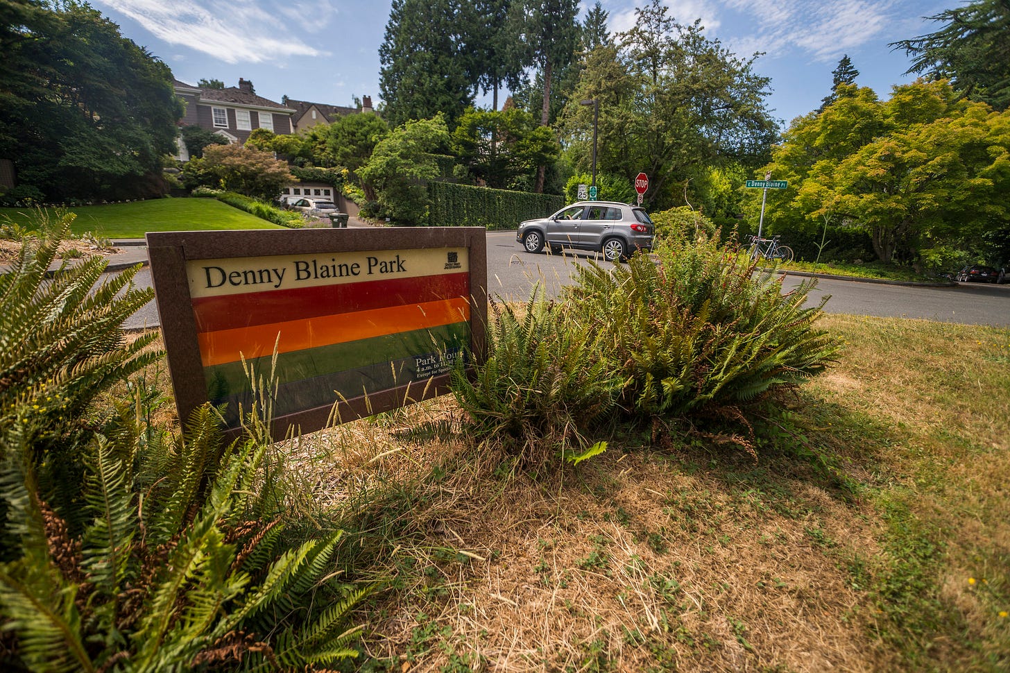 Denny Blaine Park signage with affluent suburban neighborhood in the background. Denny Blaine Park signage with affluent suburban neighborhood in the background.