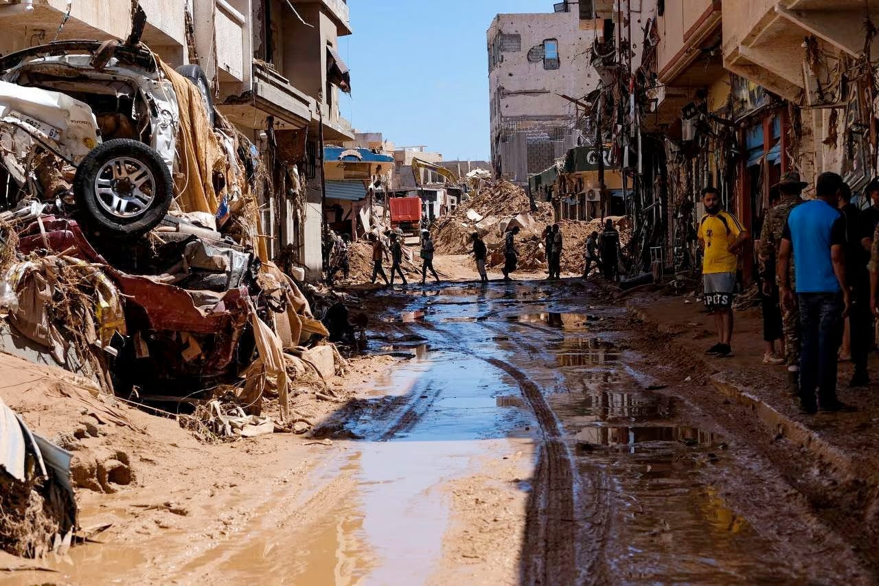 A mud drenched street in Derna, crushed cars smashed into buildings as residents wander in the destruction.