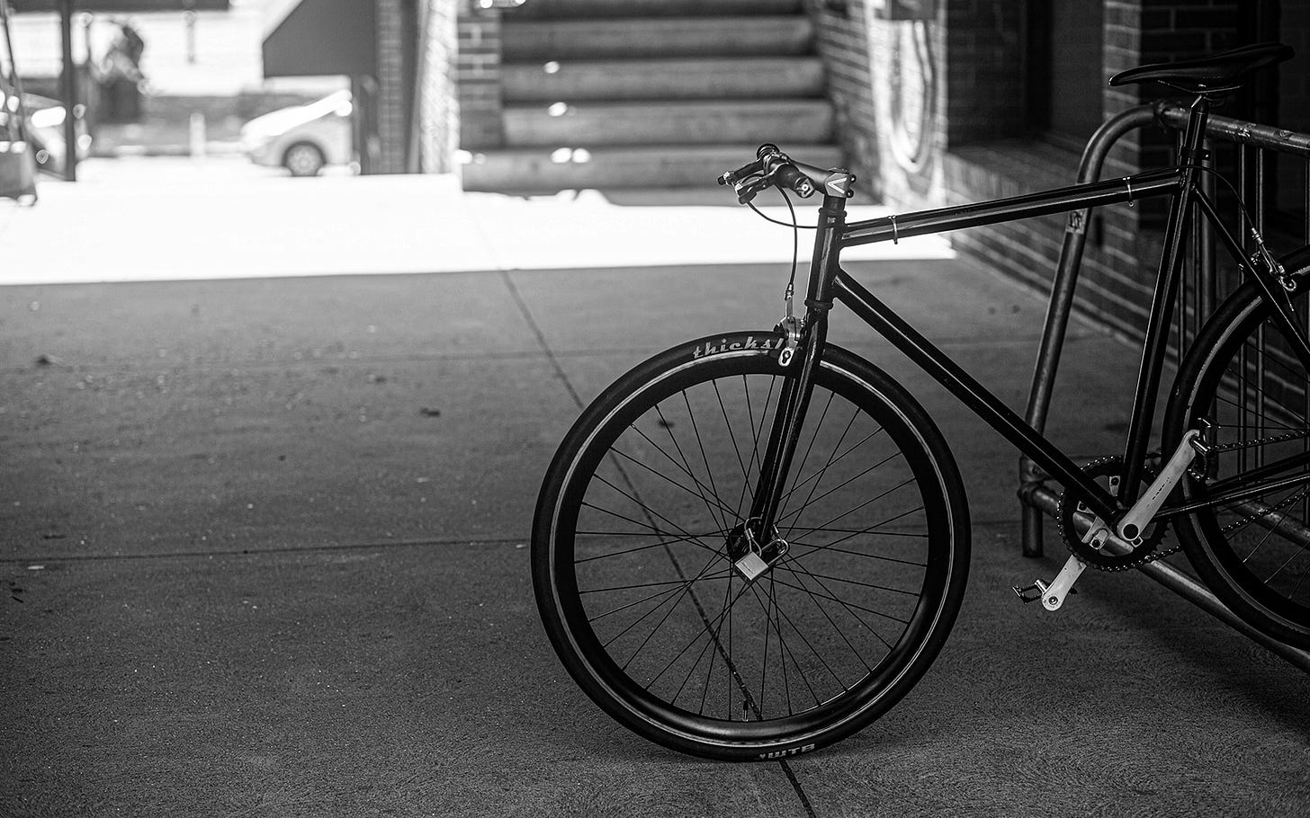 Lone bicycle rests in a stand in the shade with the bright day as a backdrop