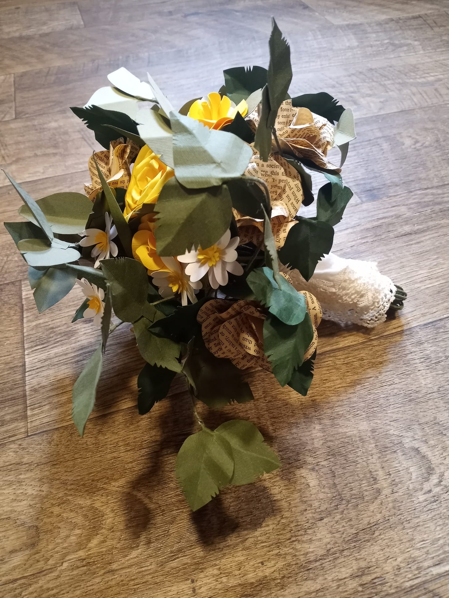 A bouquet of paper flowers, made of book paper and yellow paper made to look like roses, complete with green paper made to look like leaves