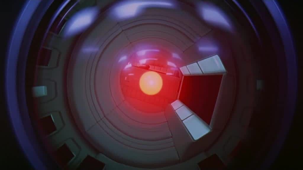 A still of HAL from 2001: A Space Odyssey, who looks like a camera lens with a red light in the center.