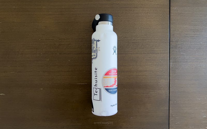 Hydroflask covered in stickers on brown table.