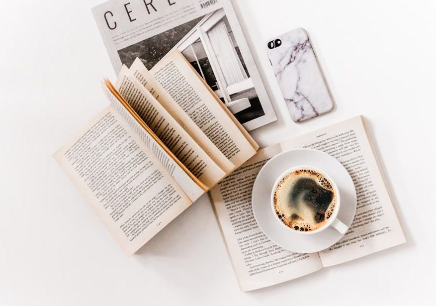 white ceramic cup with coffee on saucer beside opened books