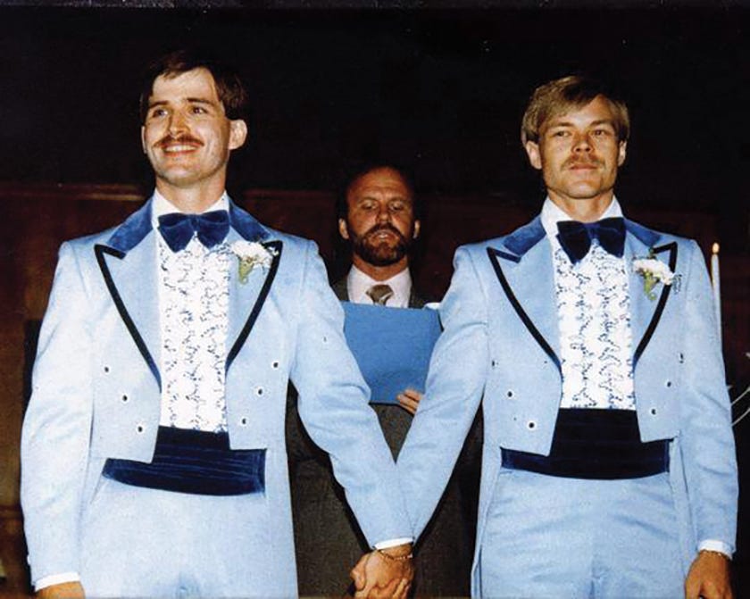 Two men in blue suits holding hands at their wedding.
