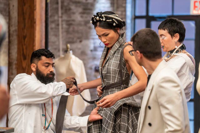 Designers Hester and Fabio constructing the grey garment on model, Mimi, as Christian Siriano watches