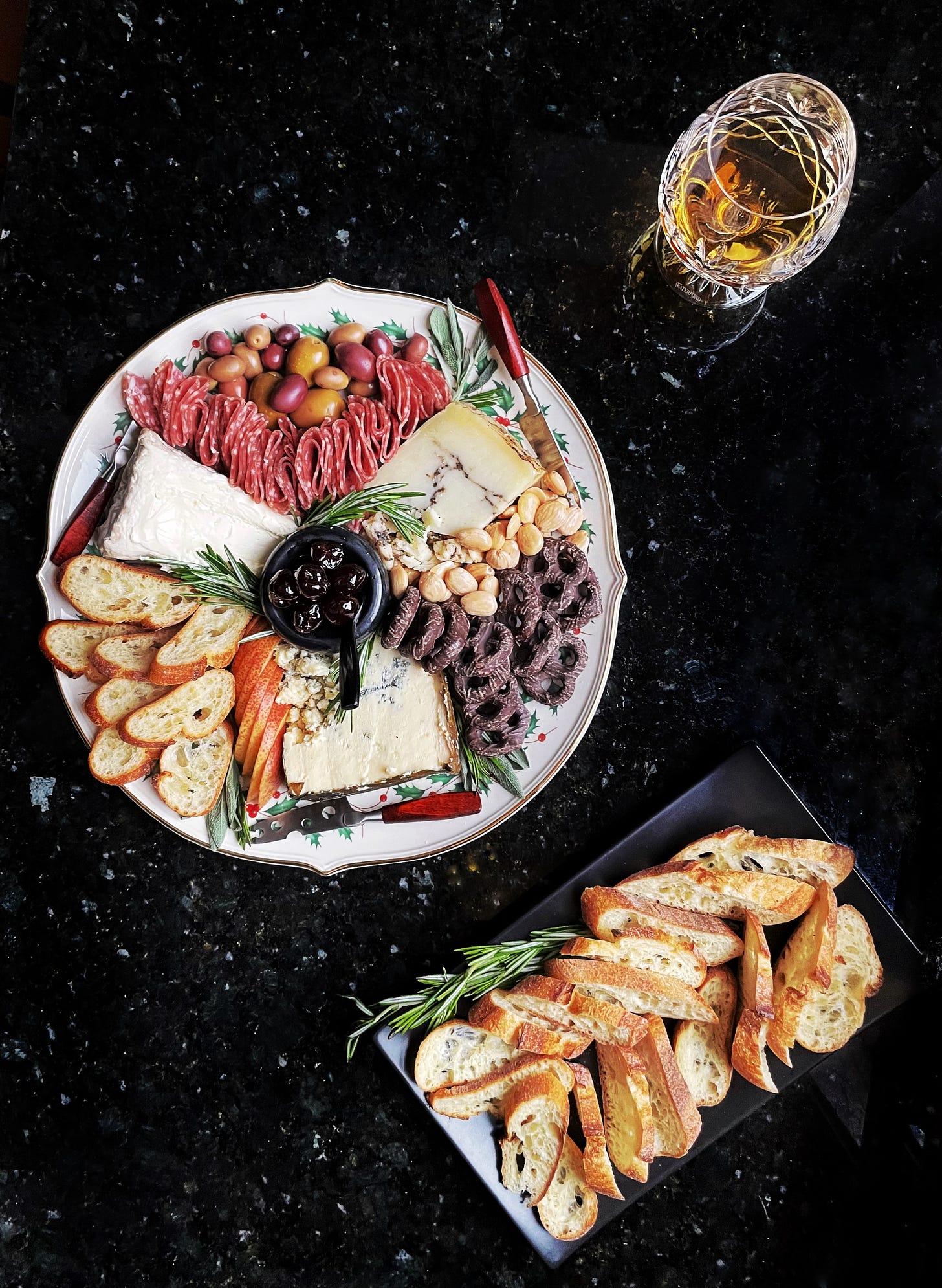 A bountiful holiday cheese plate with a glass of brandy and lots of baguette on the side