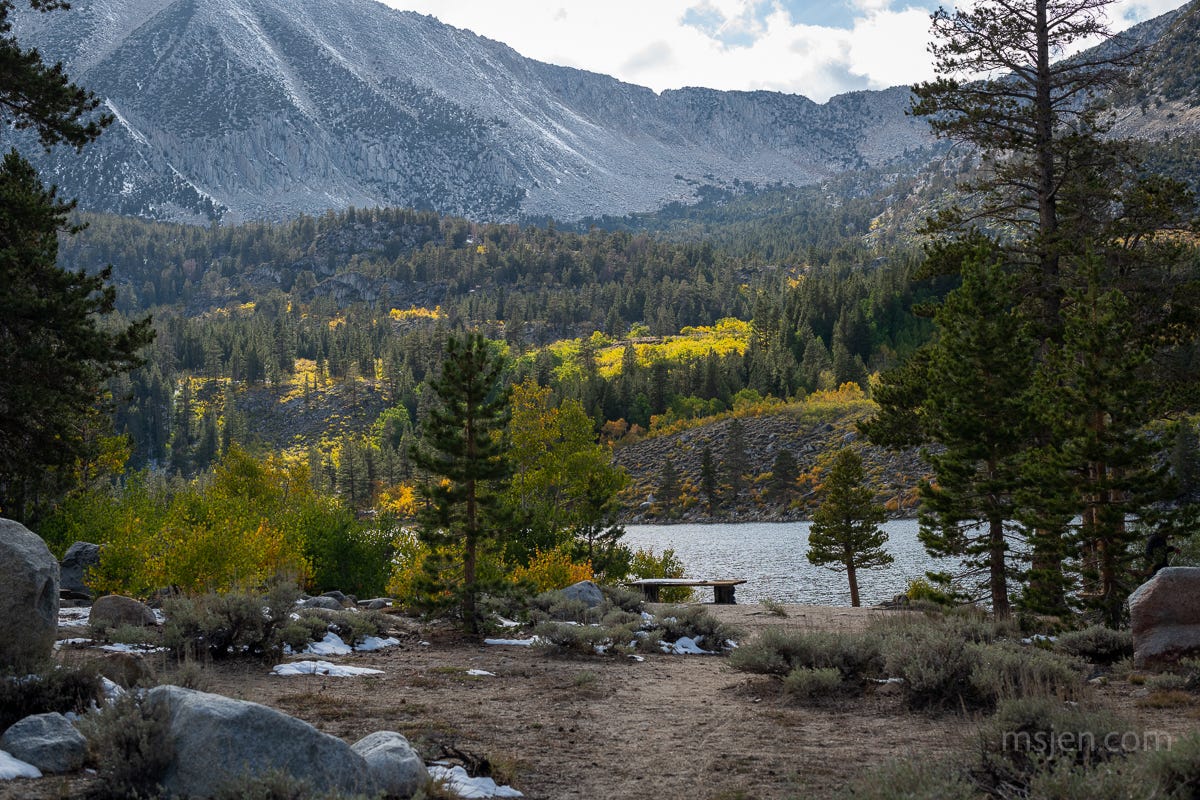 Photo a high mountain lake with pine trees and yellow aspen trees with patches of snow.