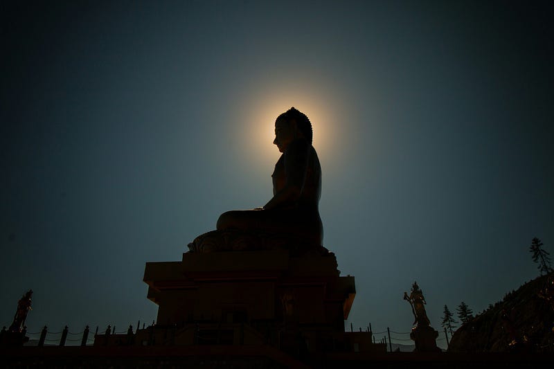 Side profile of a Buddha statue at night, the moon is positioned in the same position as its head giving a halo effect.