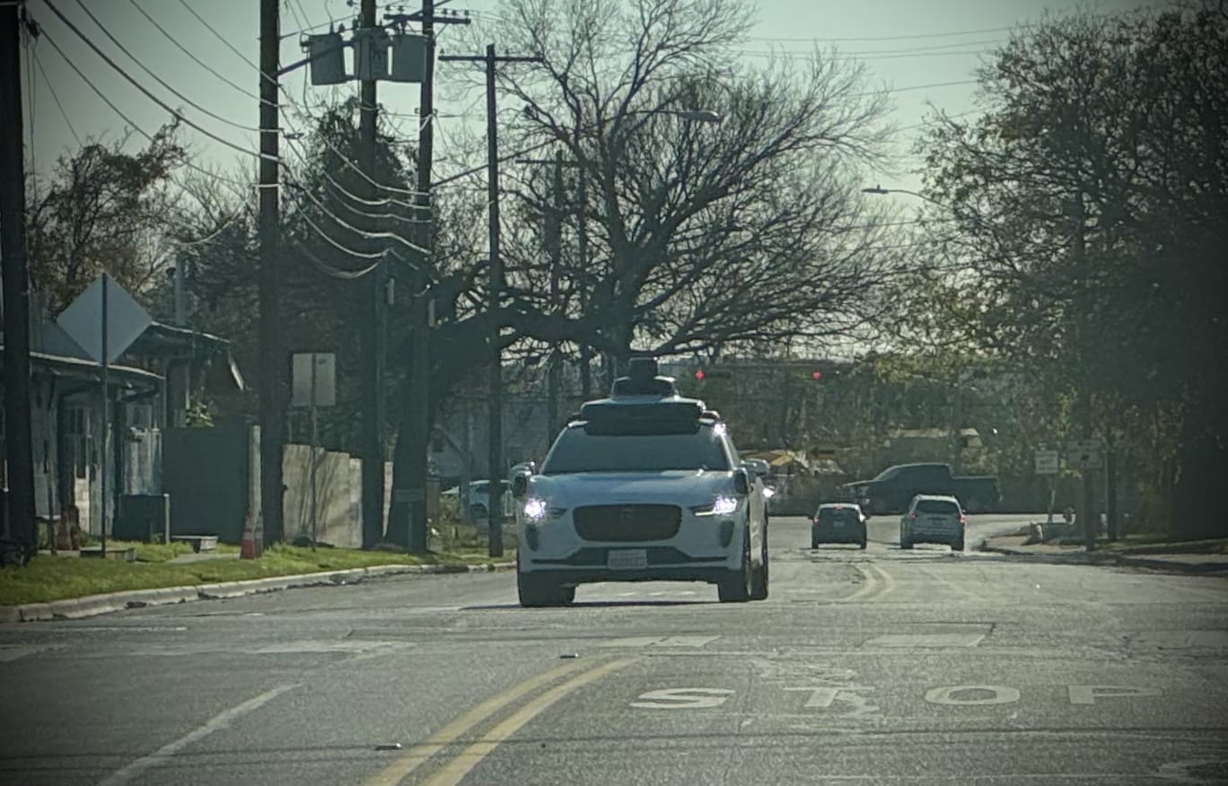 Robot taxi at a four way stop, with woods visible in the background