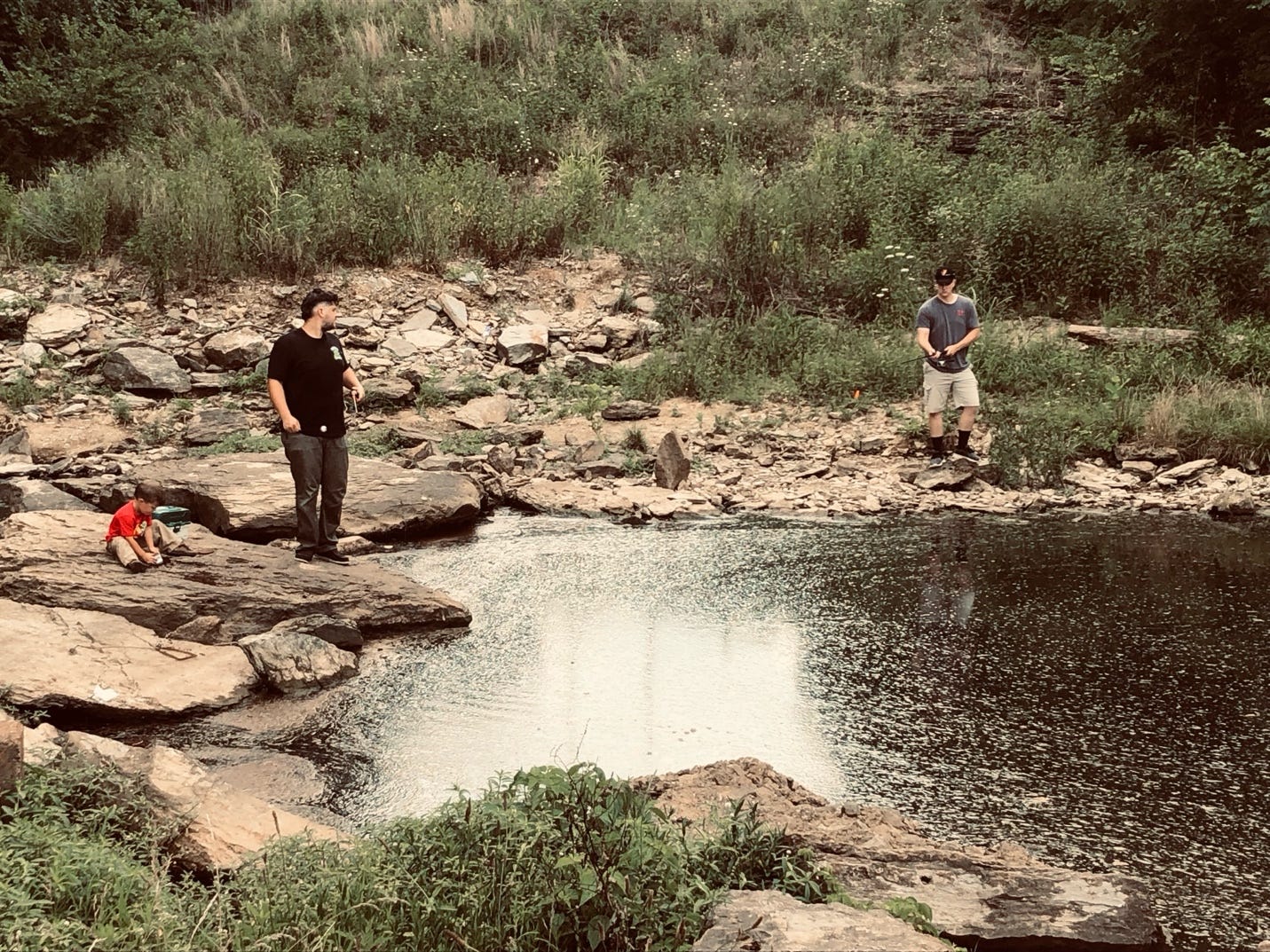 A group of men standing on rocks by a pond

Description automatically generated
