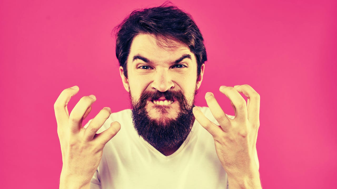An angry man holds up his hands in front of a pink background.