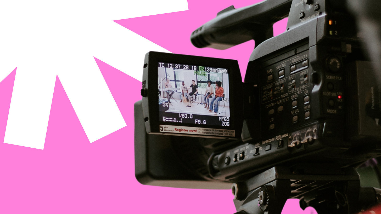 Image description: A close up of a video camera screen against a pink background and a white starburst