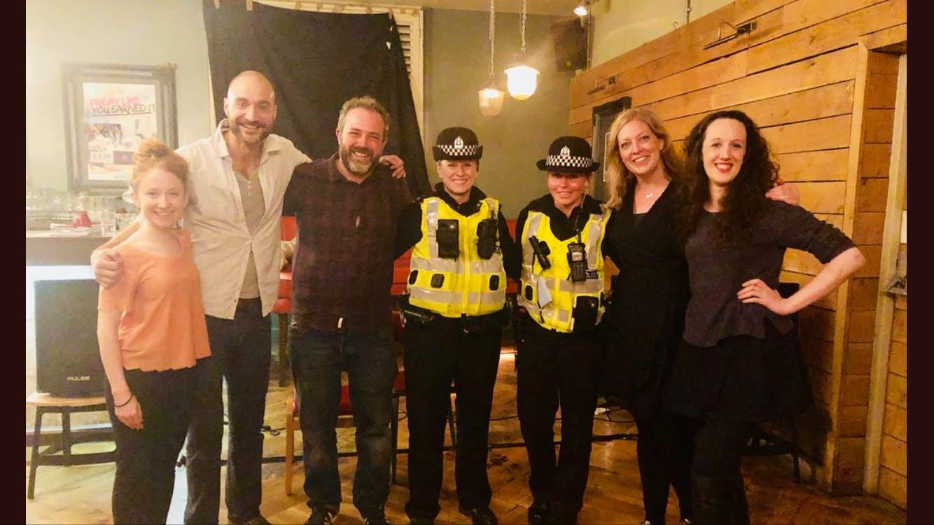 4 improvisers stand with two police women in the middle of them. All are smiling