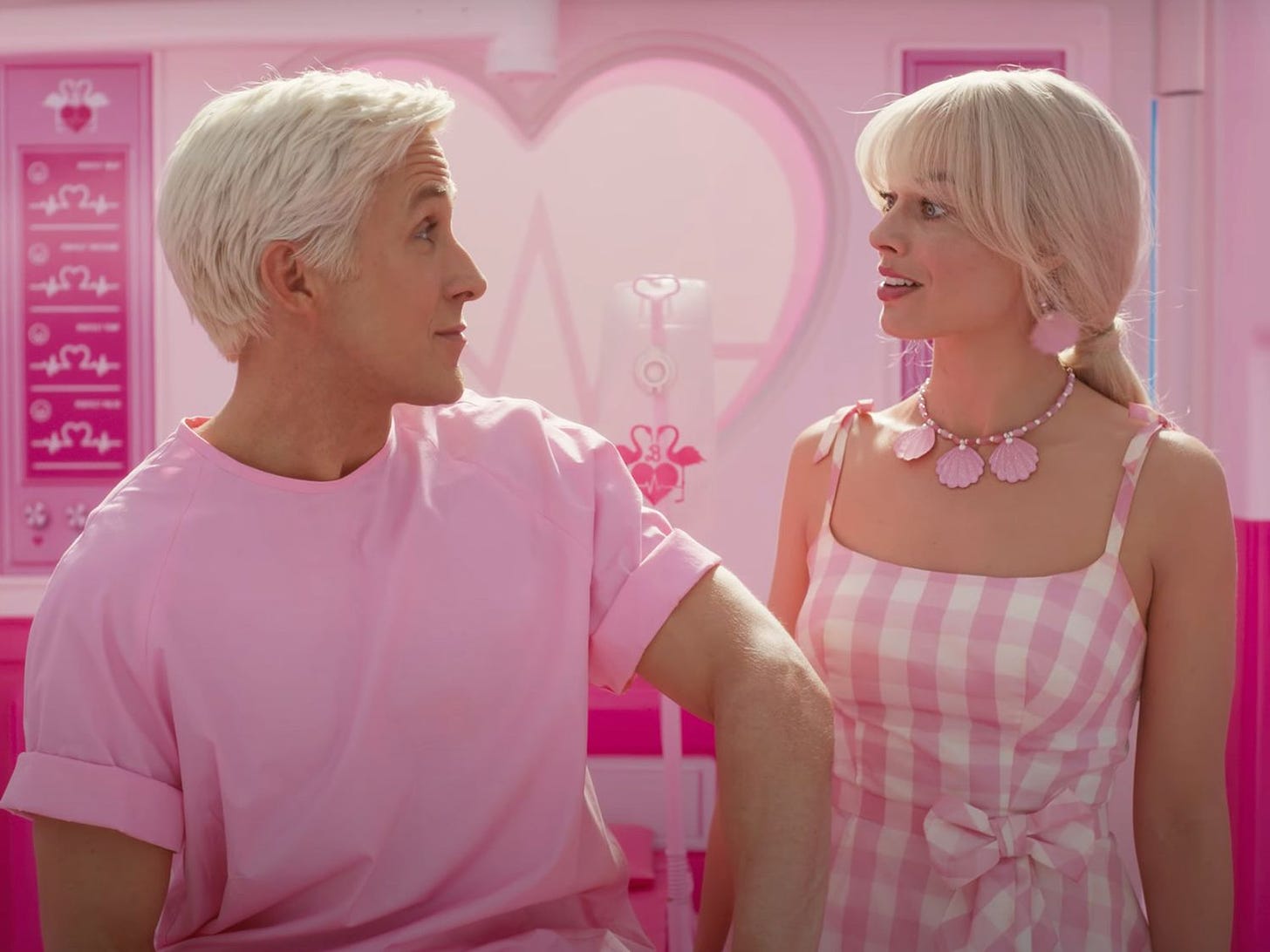 Scena del film Barbie in cui Margot Robbie e Ryan Gosling si guardano. Sono entrambi biondo platino e vestiti di rosa. Sullo sfondo c'è del mobilio rosa