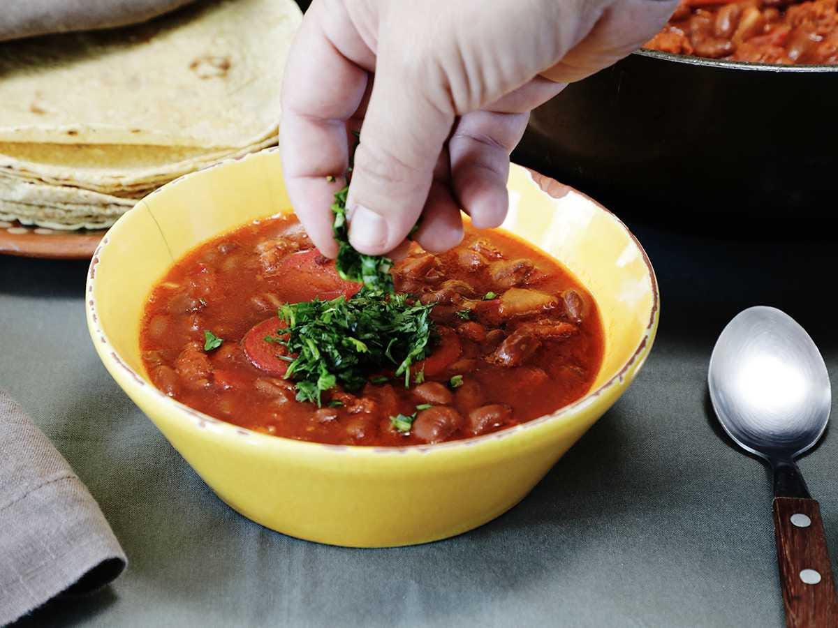 aqdding cilantro to bowl of frijoles charros