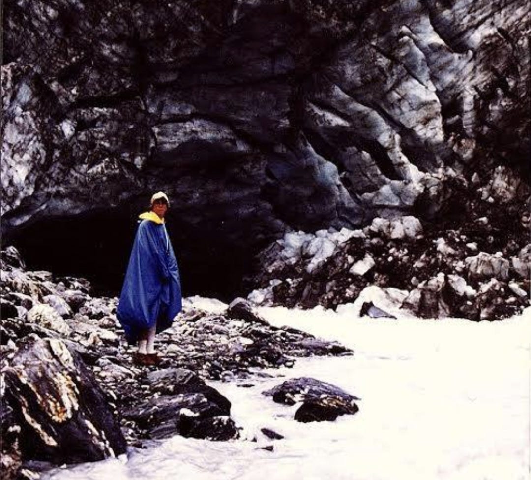 Michael wearing a blue poncho standing in front of a glacier, a river running out from the front. 