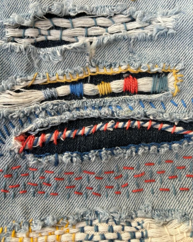 A hole in jeans patched with lots of colors of thread and different stitch methods