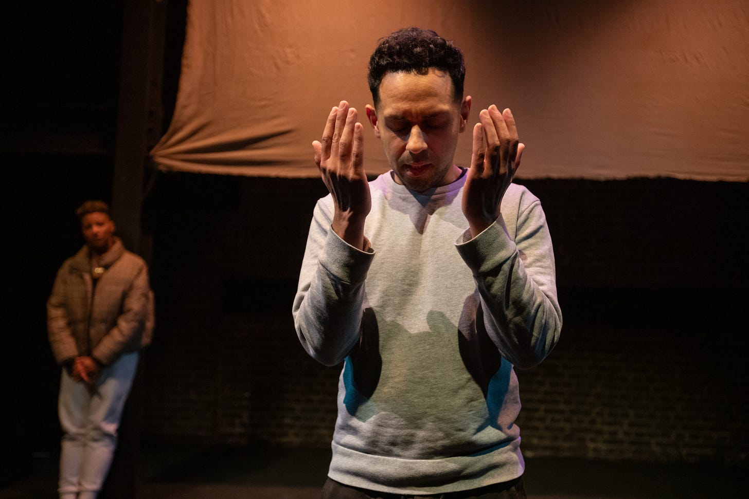 A photograph of a man in a performance of Cutting the Tightrope holding up his hands