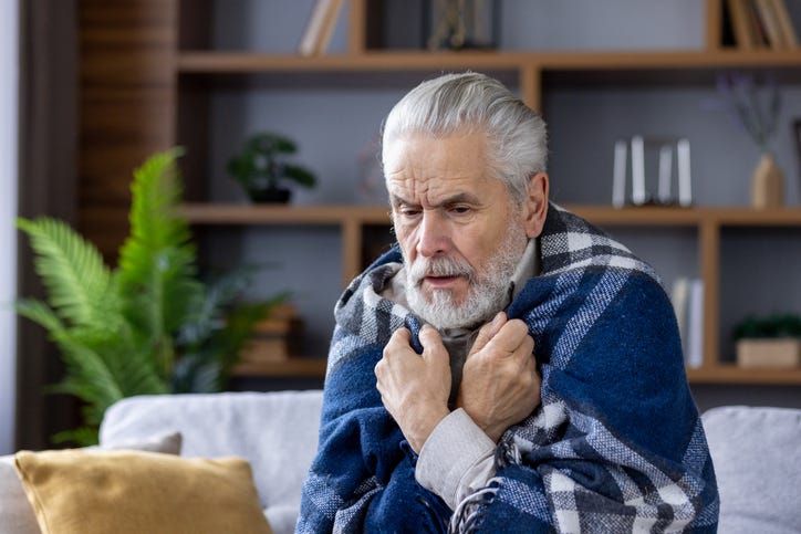 Man shivering under a blanket.