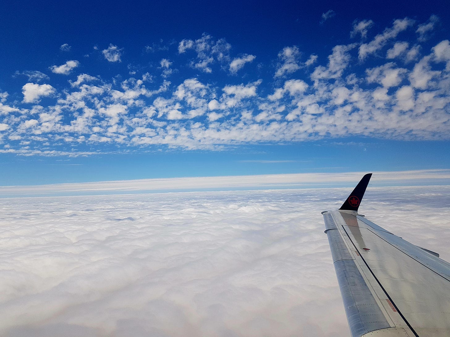 Air Canada wingtip flying above the clouds with a blue sky