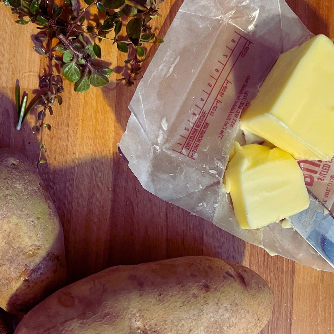 Butter and potatoes on a wooden counter top.