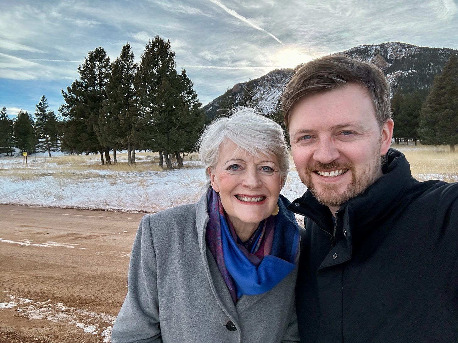 A snapshot of my mother and me in front of pine trees and a snowy mountain in the background.