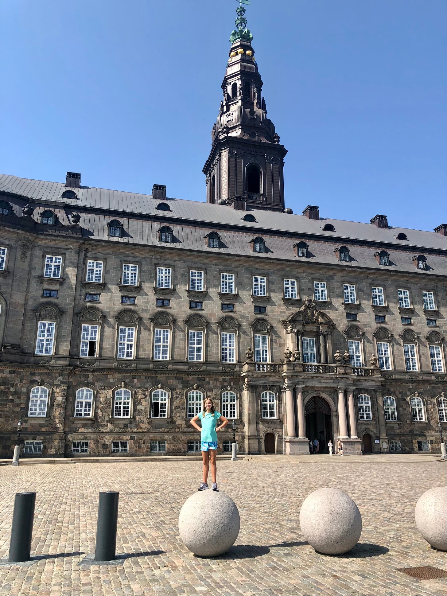 A young girl stands on top of a spherical sculpture in front of Christiansborg Palace