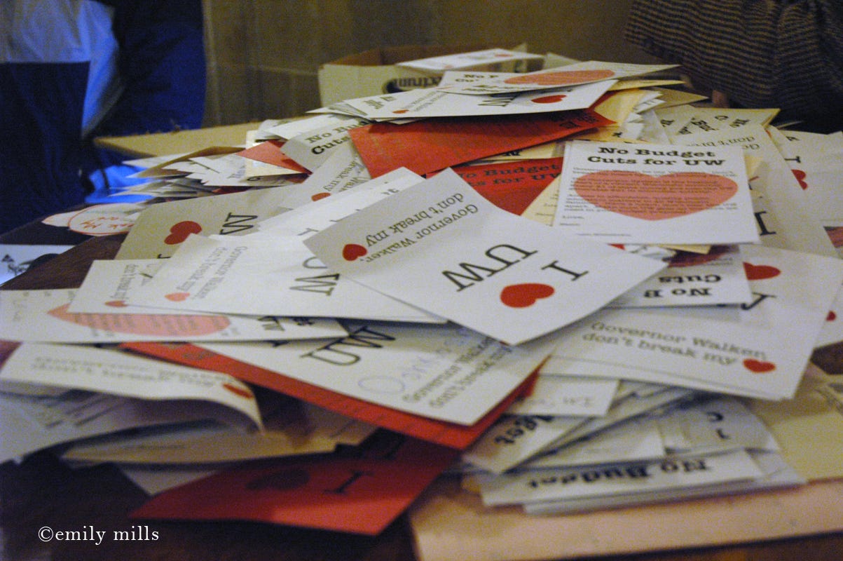 A pile of fliers that contain messages of support for the UW, reading "I Heart UW" and "No budget cuts for UW."