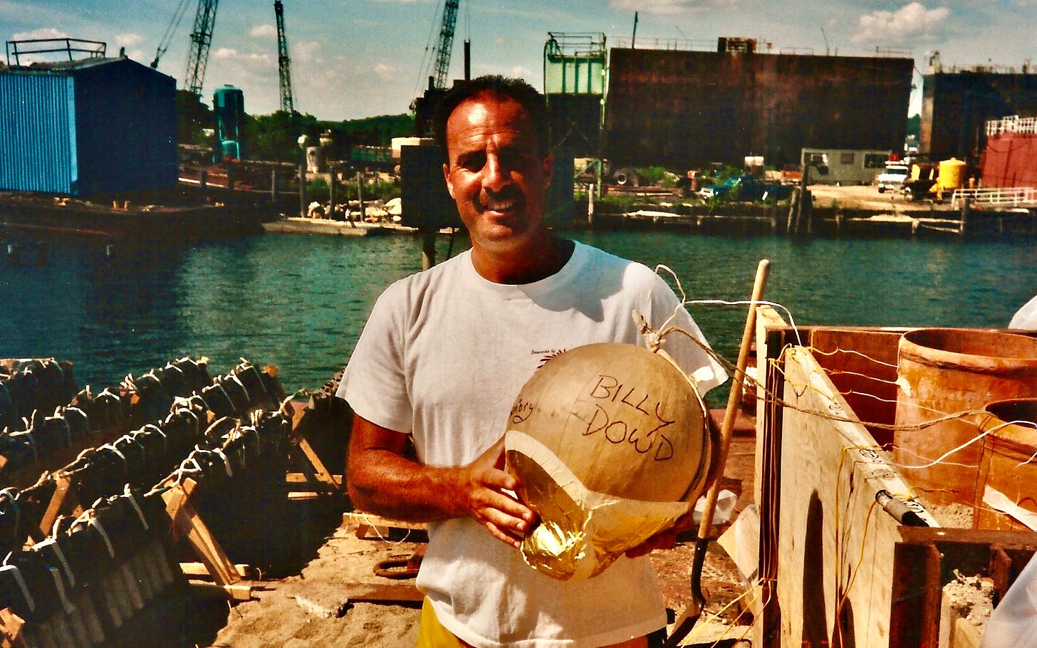 An old photo of a man on a dock holding a golden balloon-looking firework with the words Billy Dowd written on it