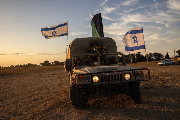 A green military vehicle, similar to a pickup truck with a canvass cover over the back, on a field of grass. It has large Israeli flags on the front bumper and passenger side.
