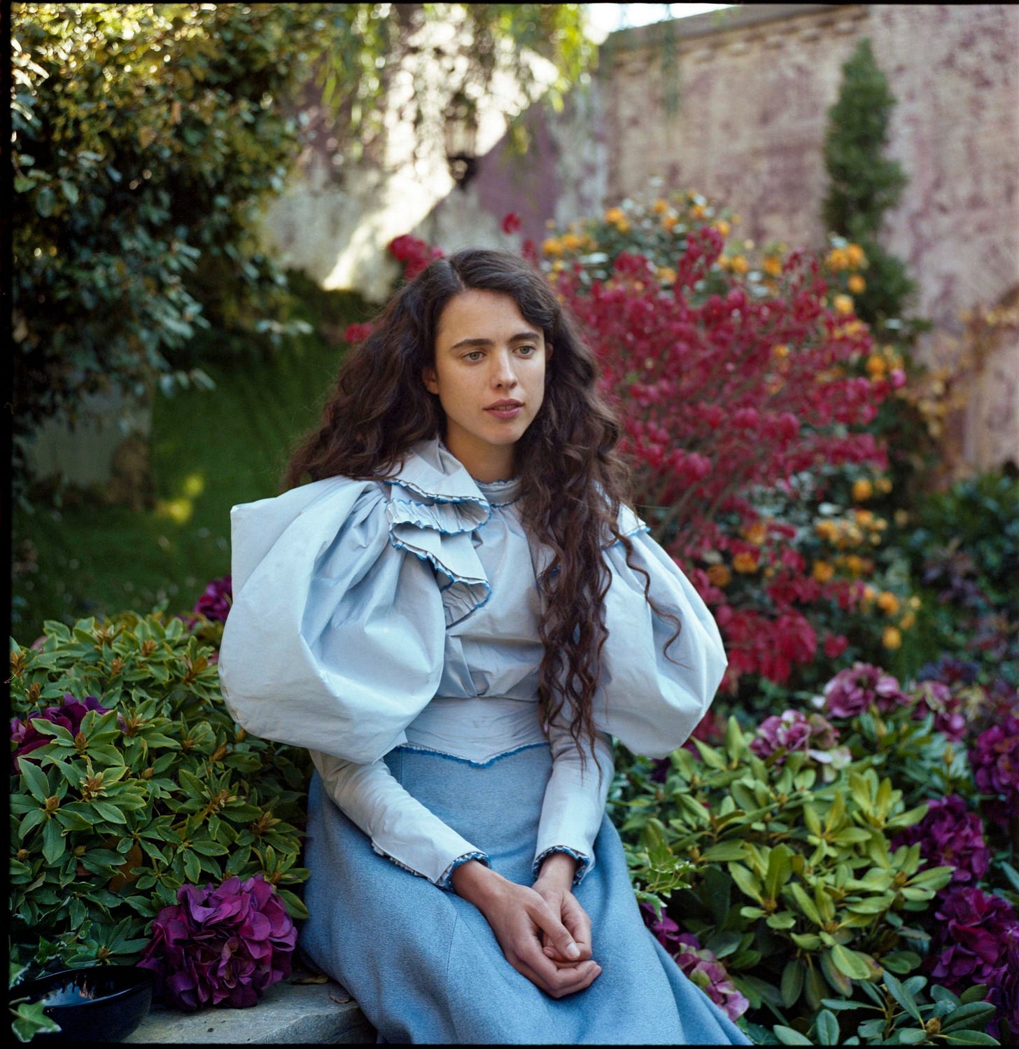 Margaret Qualley sits in a blue dress in "Poor Things" (2023)