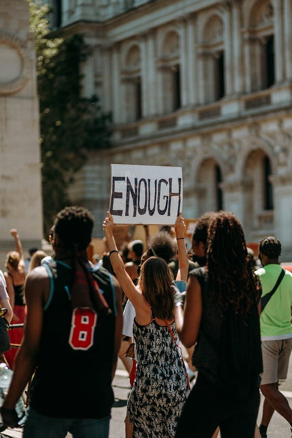 Protesters, one holds a placard with the word, “ENOUGH”. Protesters, one holds a placard with the word, “ENOUGH”.