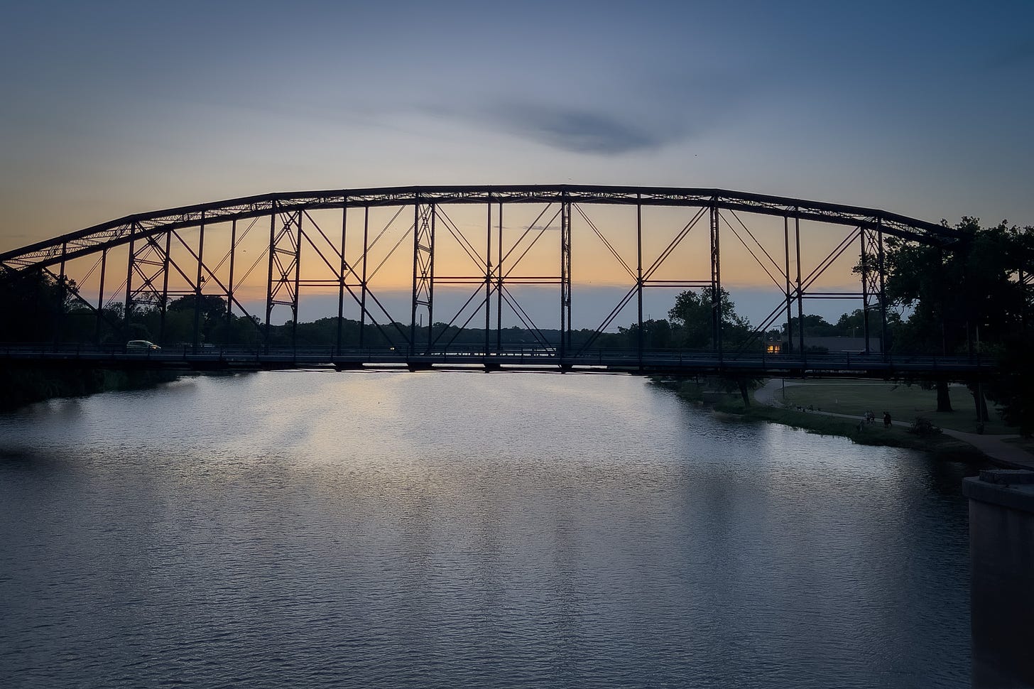 A suspension bridge casting its reflection on the river with the last rays of the setting sun in the background