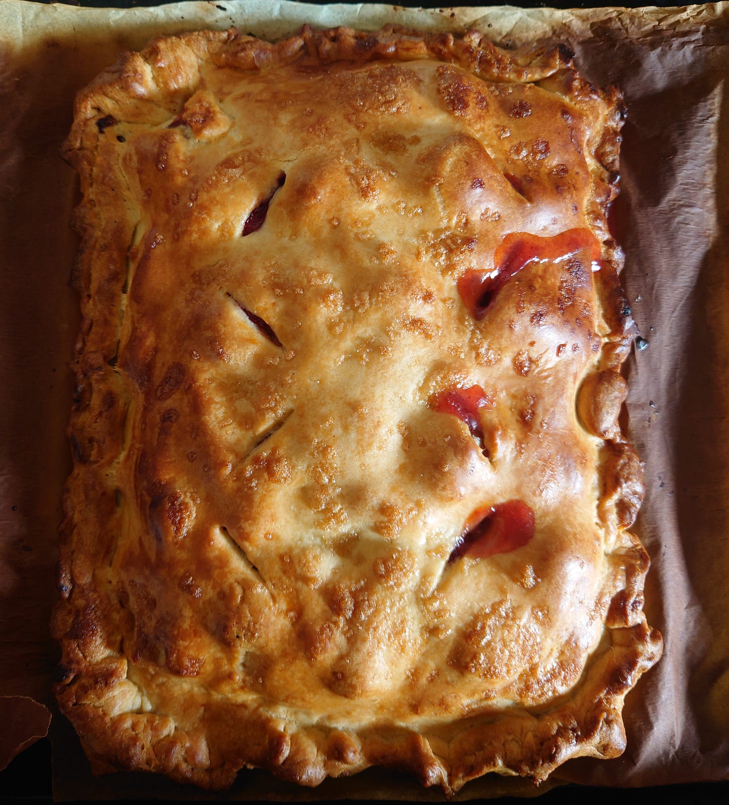 A rectangular golden-crust pie leaking red fruit juice from one of the slits in its crust, 