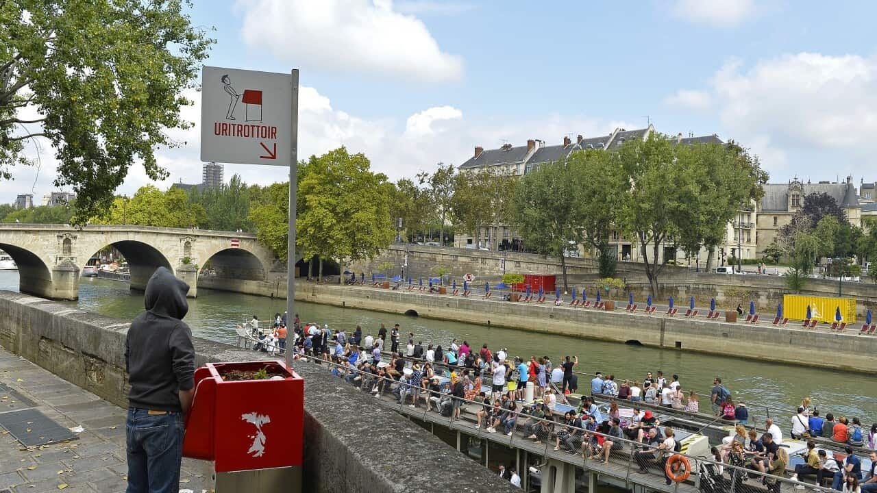 A man peeing into a public urinal next to the Seine River.