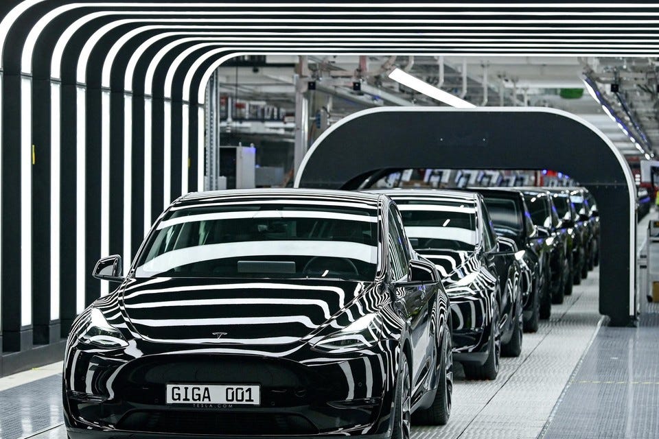 Tesla Model Y cars rolling off the production line at Tesla's Gigafactory, featuring sleek black vehicles under futuristic lighting, with 'GIGA 001' plate visible.