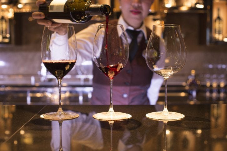 a man is serving wine into three glasses for a wine tasting event on a cruise ship which is one the the best onboard cruise activities