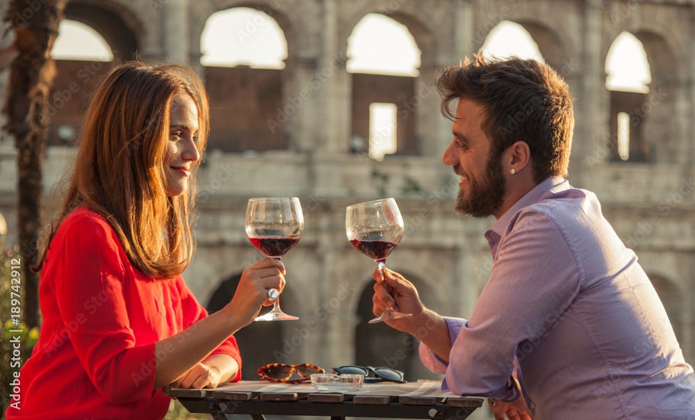 Romantic couple drinking glass of red wine sitting at restaurant table in  front of colosseum in rome at sunset. Stock Photo | Adobe Stock